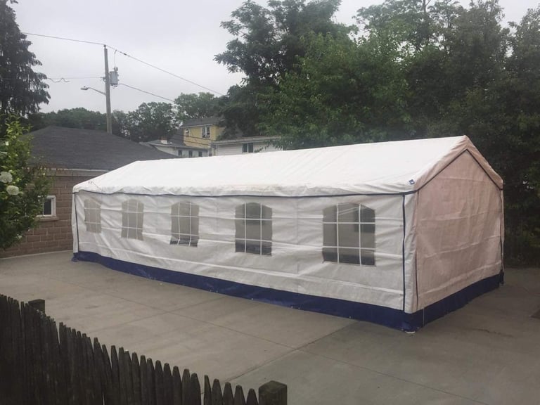 Large white and navy event tent with clear windows set up on a concrete patio in a residential backyard
