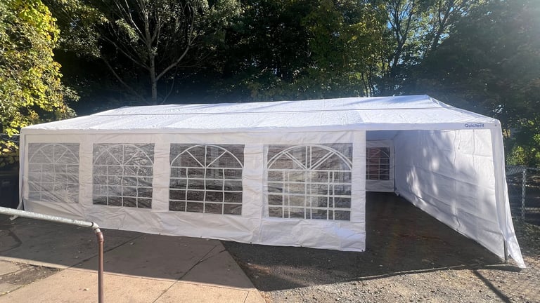White outdoor event tent with multiple large windows set up on pavement with trees in background