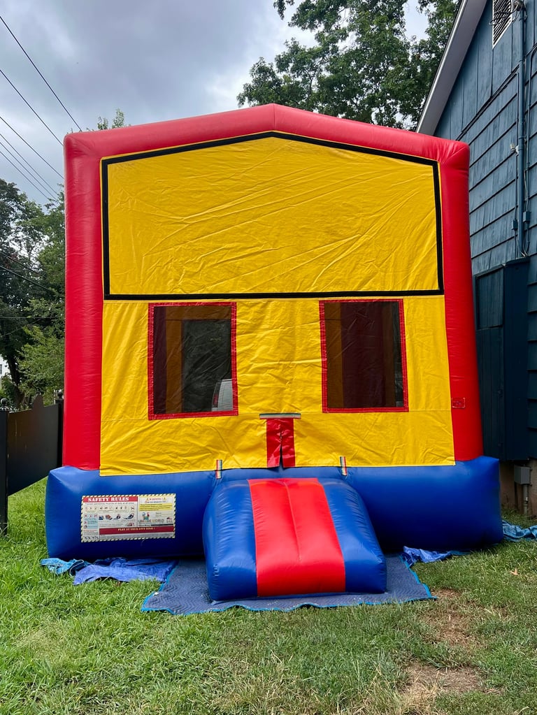 Red and yellow inflatable bounce house on grass with blue and red slide entrance