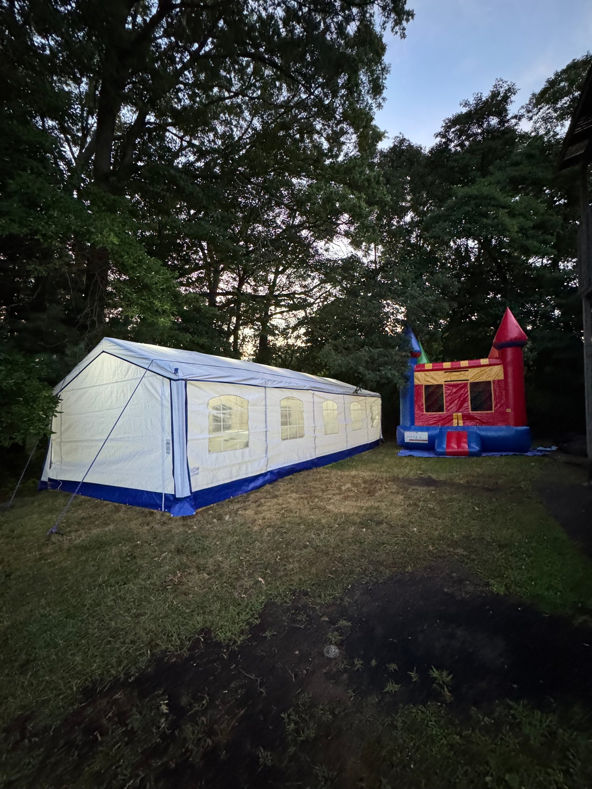 Large white and blue event tent next to a colorful red and blue bounce house in a grassy yard