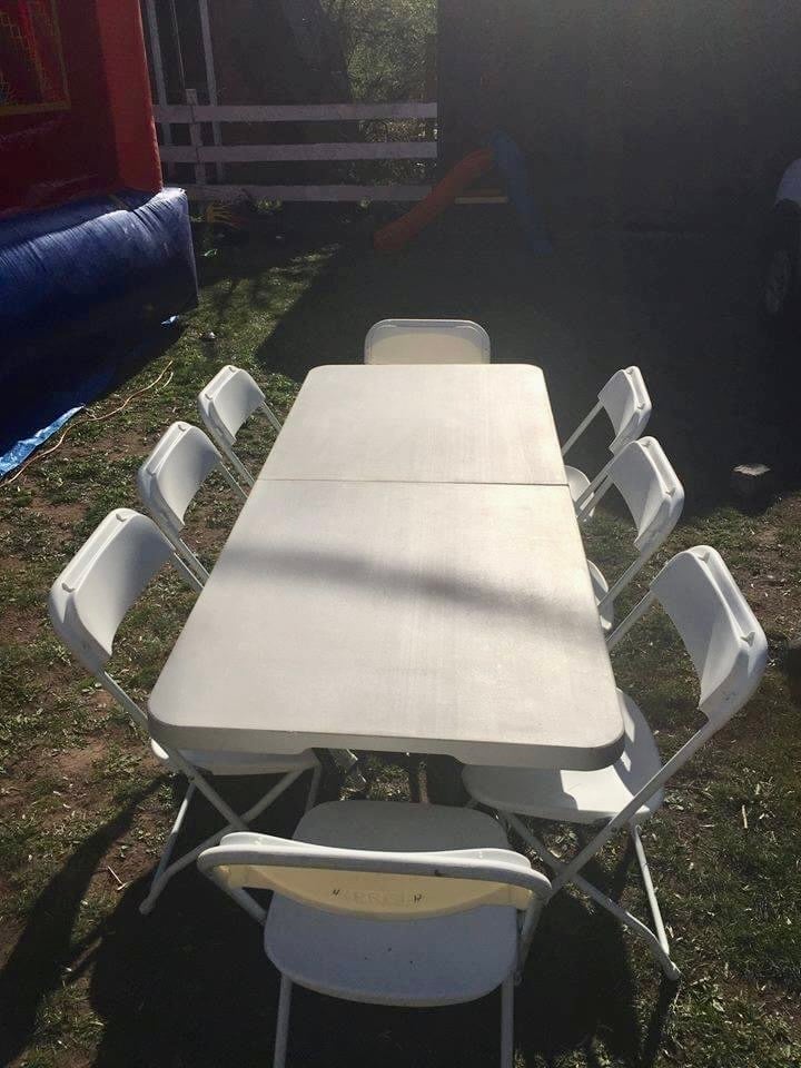 Overhead view of a white folding table with eight white plastic chairs arranged around it outdoors on grass